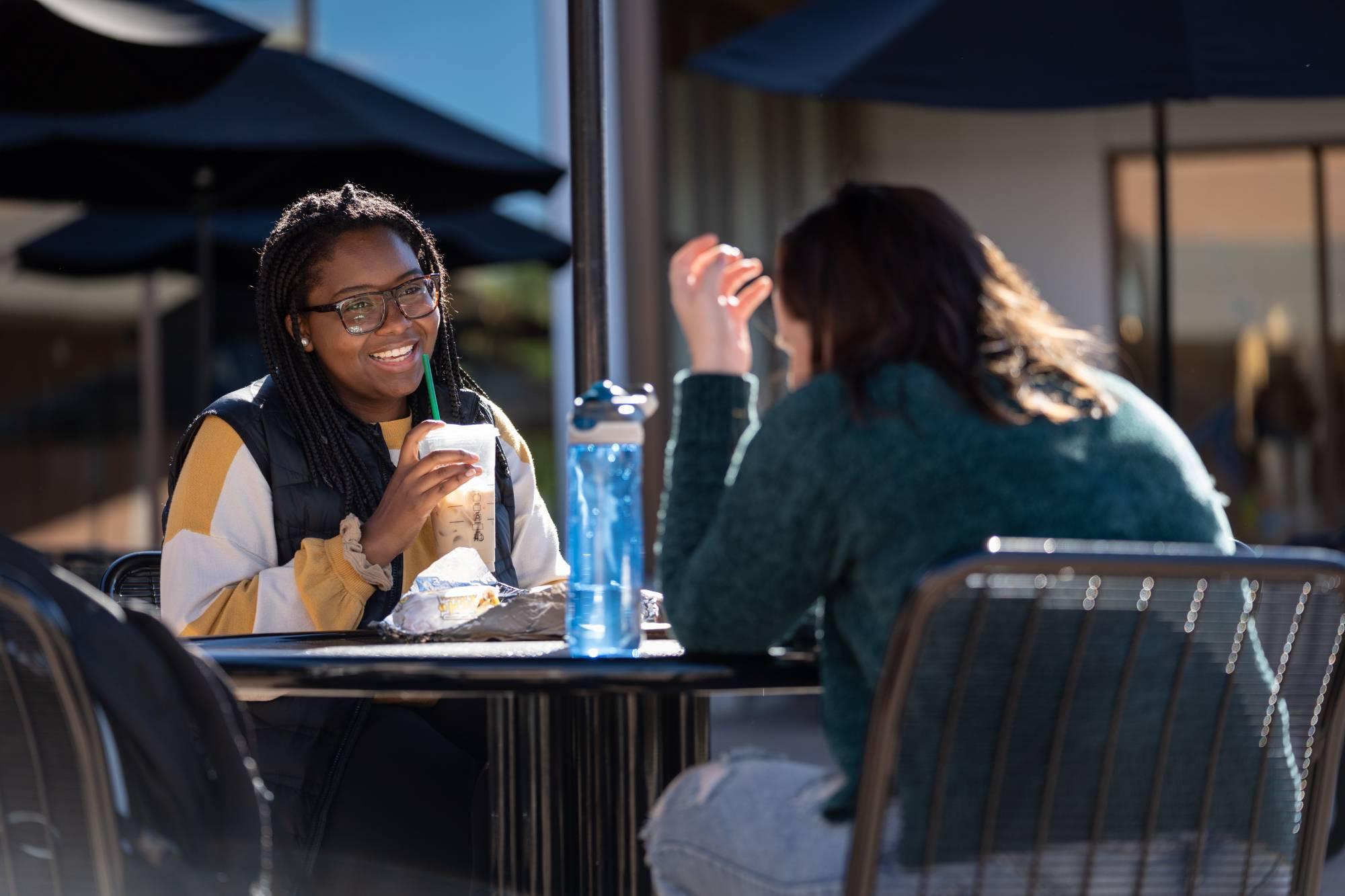 Students sitting at a table laughing and drinking coffee